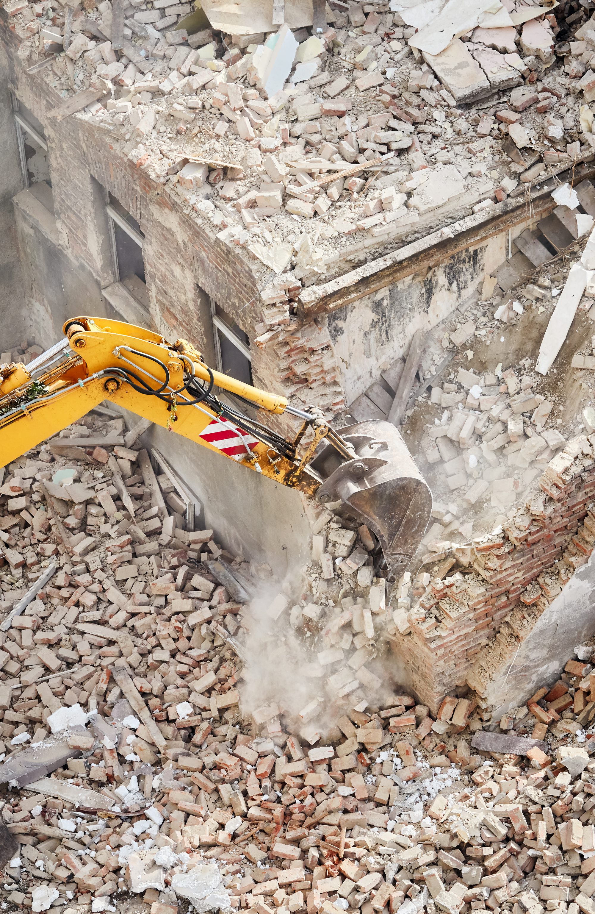 A yellow excavator breaking concrete in a cloud of dust